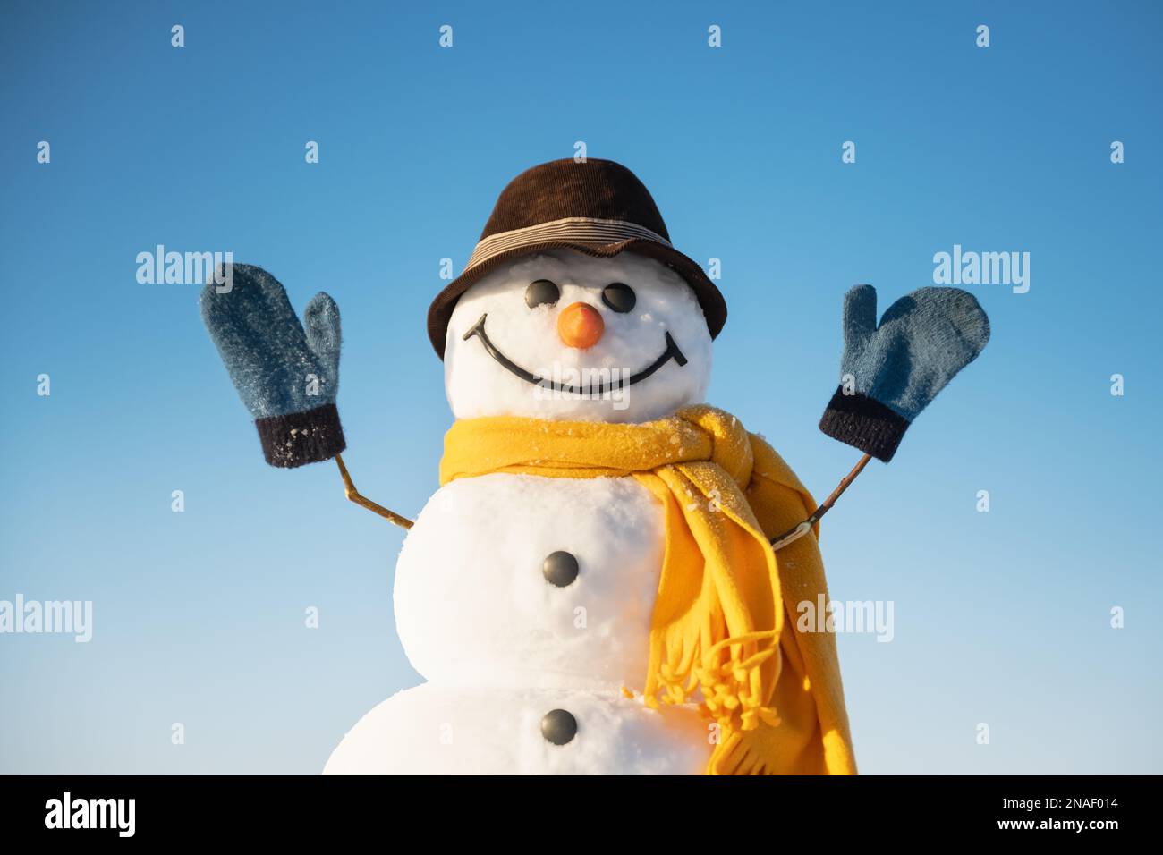 Lustiger Schneemann mit braunem Hut und gelbem Kopftuch mit Händen oben auf blauem Himmelshintergrund Stockfoto