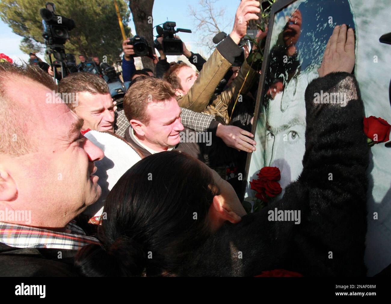 People react near to large photos of those who died a year ago, during a peaceful anti-government demonstration in front of the main government building of Albanian Prime Minister Sali Berisha, in Tirana, Saturday Jan. 21, 2012. Opposition supporters placed flower tributes and candles to honour the dead demonstrators during the peaceful march to mark the year anniversary in the capital Tirana on Saturday.(AP Photo/Hektor Pustina) Stockfoto