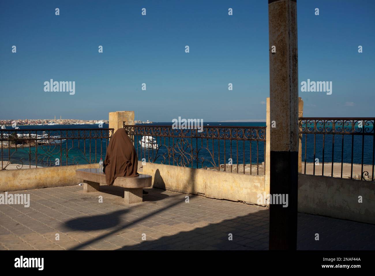 Muslimische Frau in braunem Niqab, wartet und sitzt am Roten Meer Stockfoto