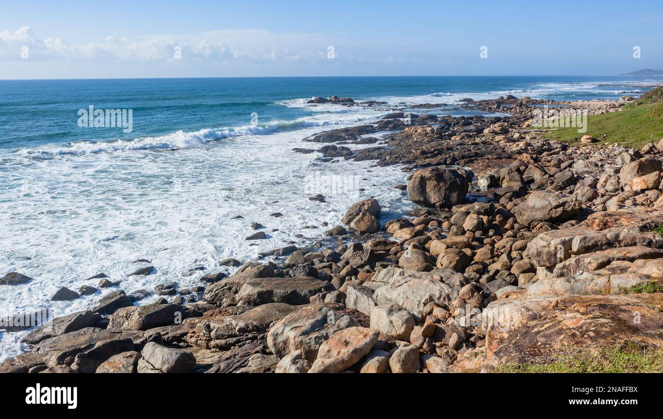 Malerische felsige Küste mit brechenden Meereswellen und Blick auf landschaftlich reizvolle Strandferienlandschaft. Stockfoto