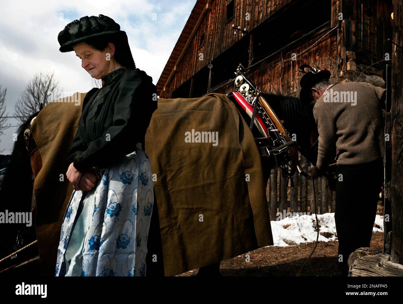 Mit schwarzem Hut wartet eine Schwester, während ihr Bruder ein Pferd vom Schlitten aushängt. Einige Ladinos wählen ein einfaches Leben in Laval, den Dolomiten, eine Zunge... Stockfoto