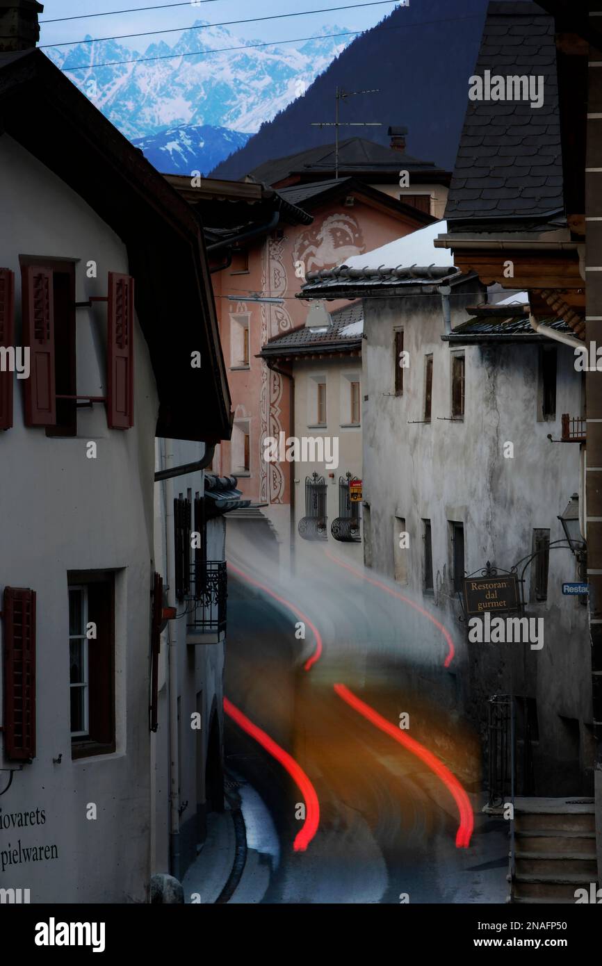 Die Rücklichter verwischen, während ein Bus durch das Gebäude in den engen Gassen des Schweizer Dorfes Santa Maria quetscht. Der Charme der Berggemeinden... Stockfoto