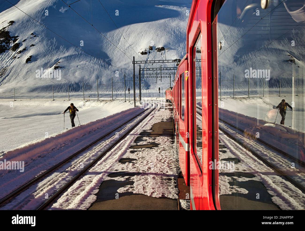 Skilanglauf durchquert eine verschneite Strecke in der Nähe des Zuges, die durch die spektakuläre Alpenlandschaft führt und 55 Tunnel und 196 Brücken durchquert Stockfoto