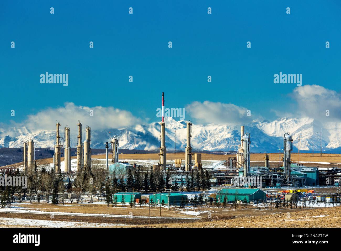 Gaskraftwerk im Winter mit schneebedeckten felsigen Bergen im Hintergrund mit blauem Himmel und Wolken über den Bergen, nördlich von Cochrane Stockfoto
