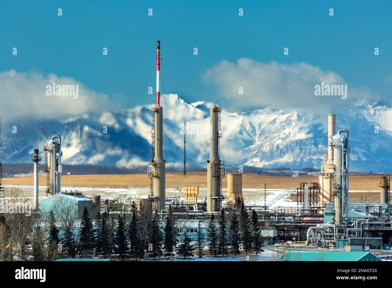 Gaskraftwerk im Winter mit schneebedeckten felsigen Bergen im Hintergrund mit blauem Himmel und Wolken über den Bergen, nördlich von Cochrane Stockfoto