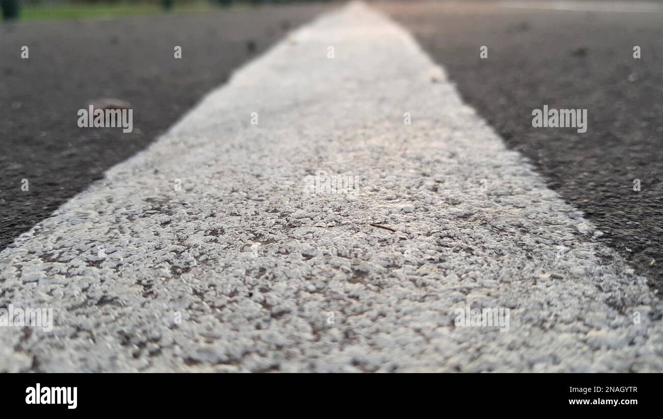 Straßenoberfläche mit weißer Nahaufnahme. Textur von grauem Asphalt und Nahaufnahme von Straßenmarkierungen. Freier Blick auf den Sportbereich des Stadions. Stockfoto