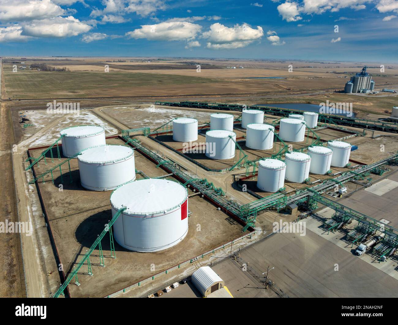 Aus der Vogelperspektive der großen runden Metallöllagertanks mit Rohrleitungen, die sie mit blauem Himmel und Wolken verbinden, westlich von Carseland, Alberta Stockfoto