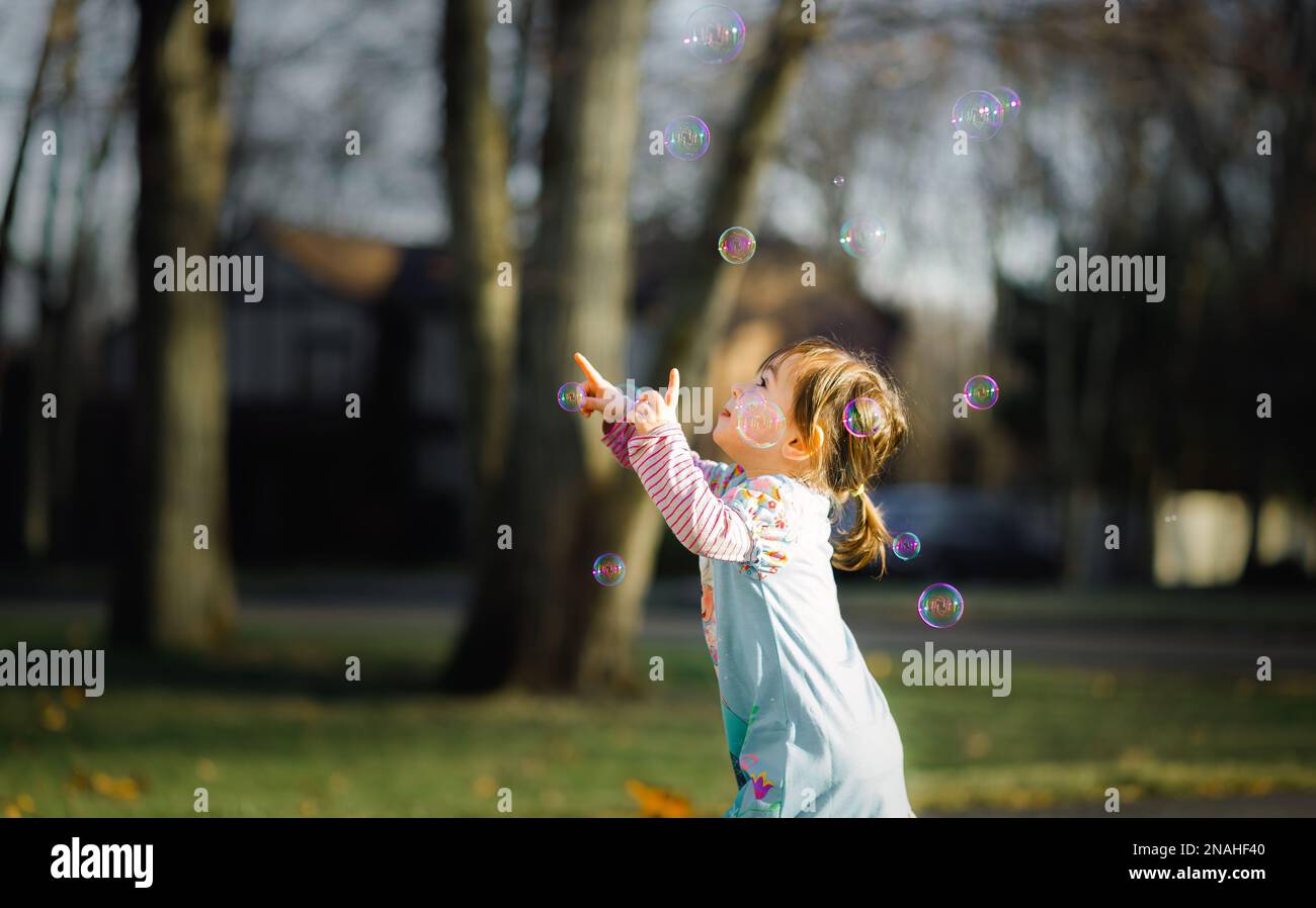 Kleinkinder spielen mit bunten Blasen in warmem Sonnenlicht Stockfoto