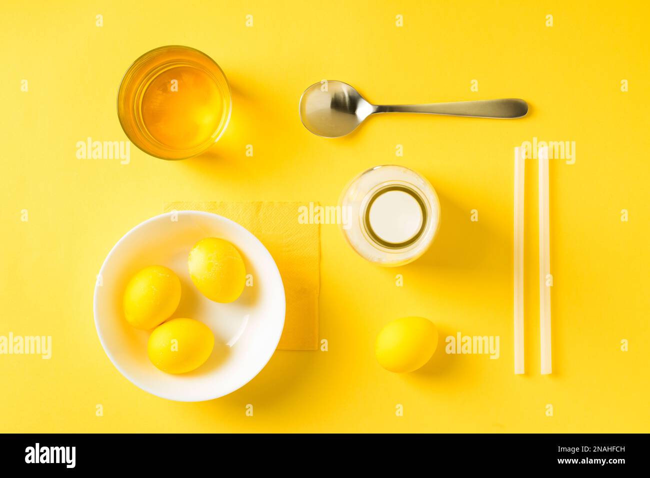 Gelb gefärbte ostereier, Löffel, Milch, Stroh und Lebensmittelfarbe auf flacher Tischplatte. Stockfoto