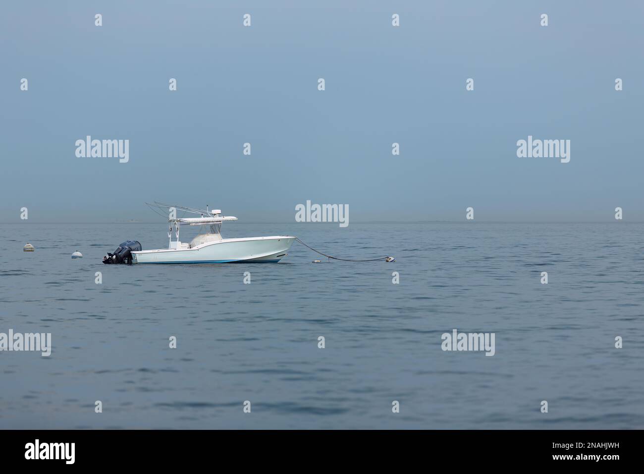 Weißes Boot, das allein im Meer vor stürmischem grauen Himmel verankert ist Stockfoto