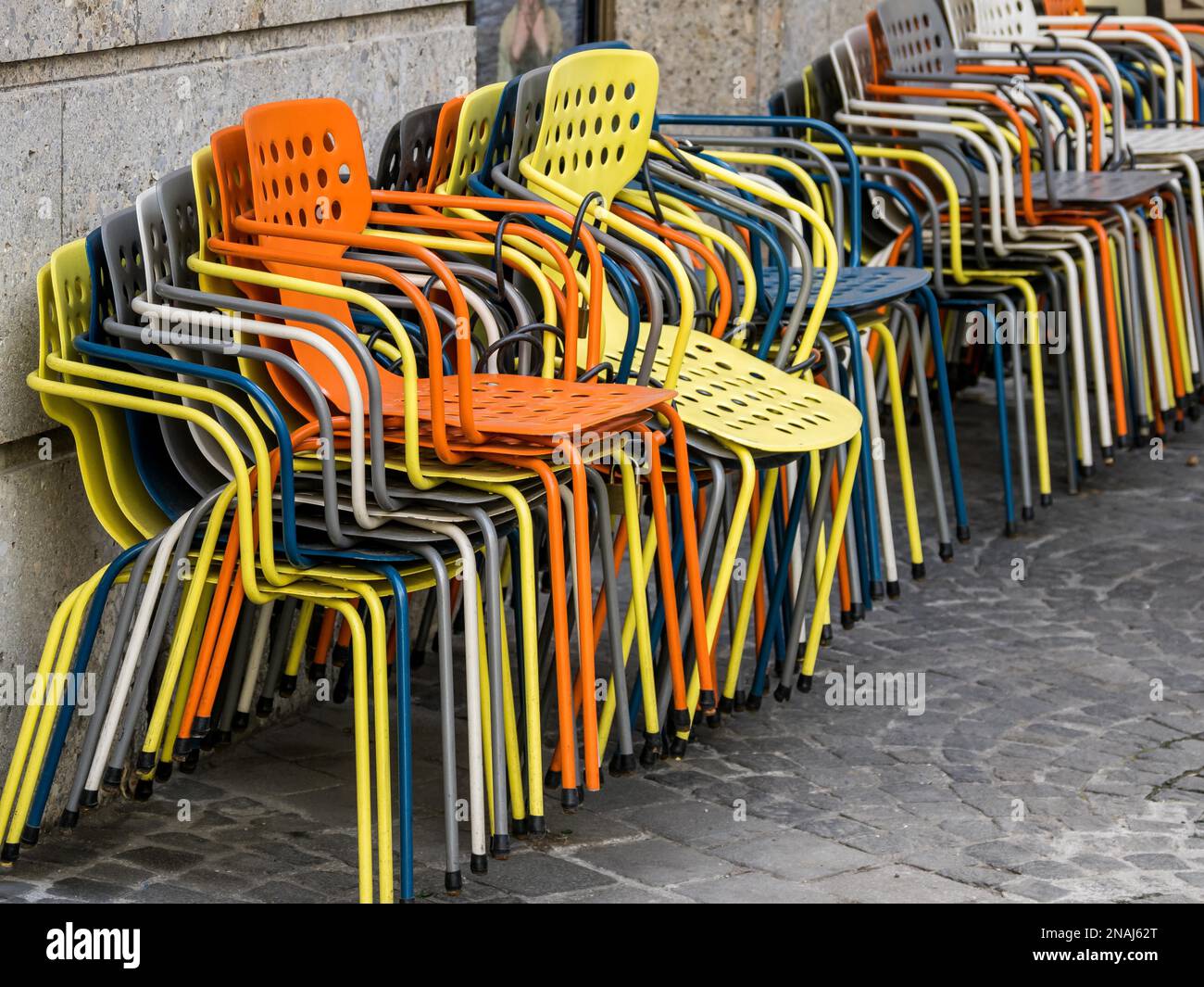 In einem Restaurantgarten sind farbenfrohe Sessel gestapelt. Symbol für Sperrung, Schließung und Ruhetag. Tourismuskrise Stockfoto