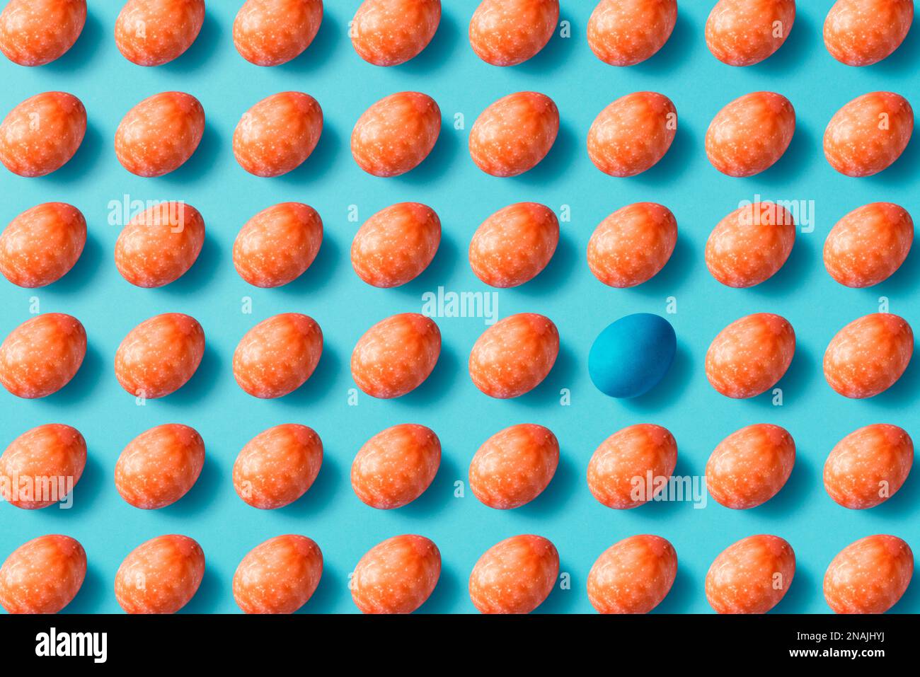 Rote ostereier auf blauem Hintergrund. Ein blaues Ei, das hervorsticht. Tischplatte flach liegend. Stockfoto