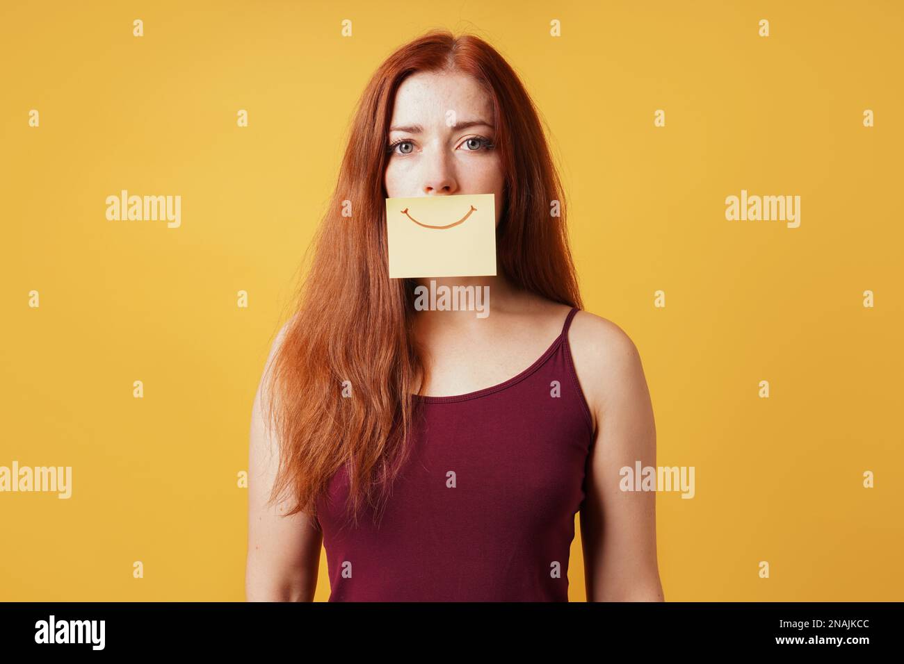 Junge Frau versteckt Traurigkeit oder Depression hinter gefälschten Lächeln gezeichnet Auf gelbem Haftnotizpapier Stockfoto