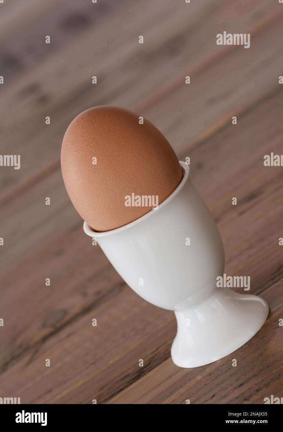 Frühstücksei in einem weißen Eierbecher befindet sich auf dem Holztisch, vertikales Format Stockfoto