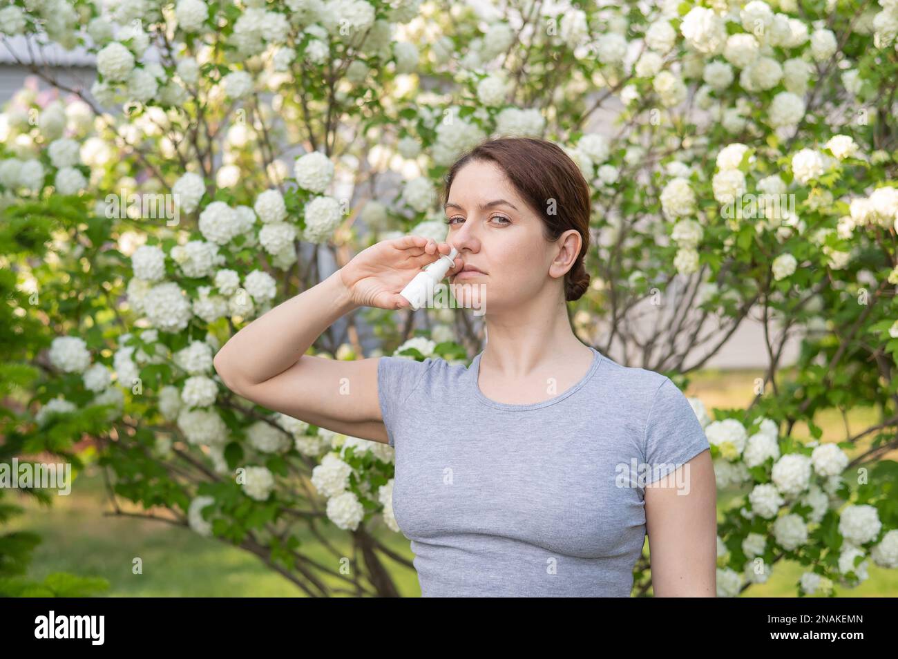 Kaukasische Frau verwendet ein Nasenspray, während sie im Park spazieren geht. Stockfoto