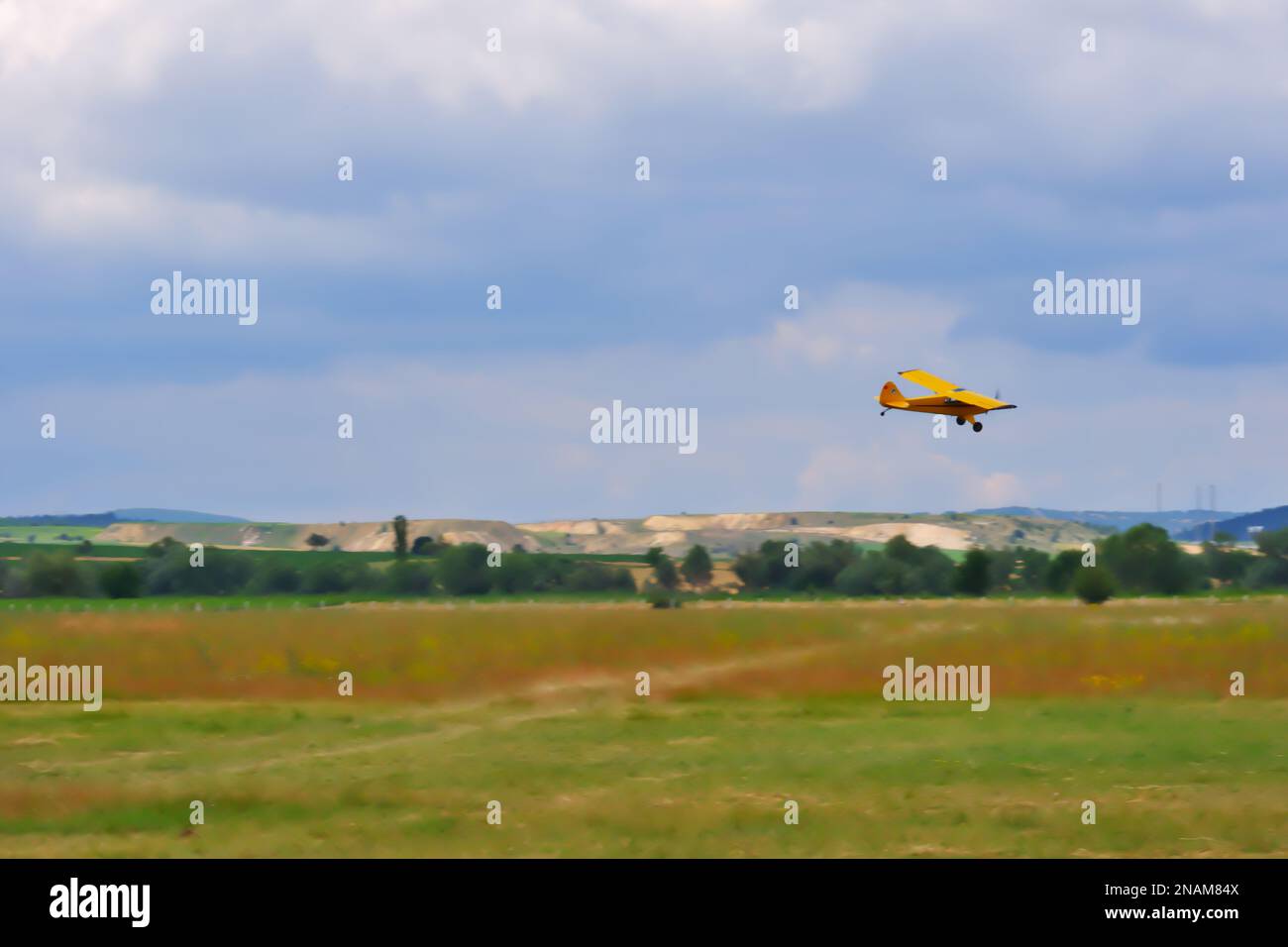 Gelbes einmotoriges Flugzeug manövriert nahe am Boden mit bewölktem Himmel im Hintergrund Stockfoto