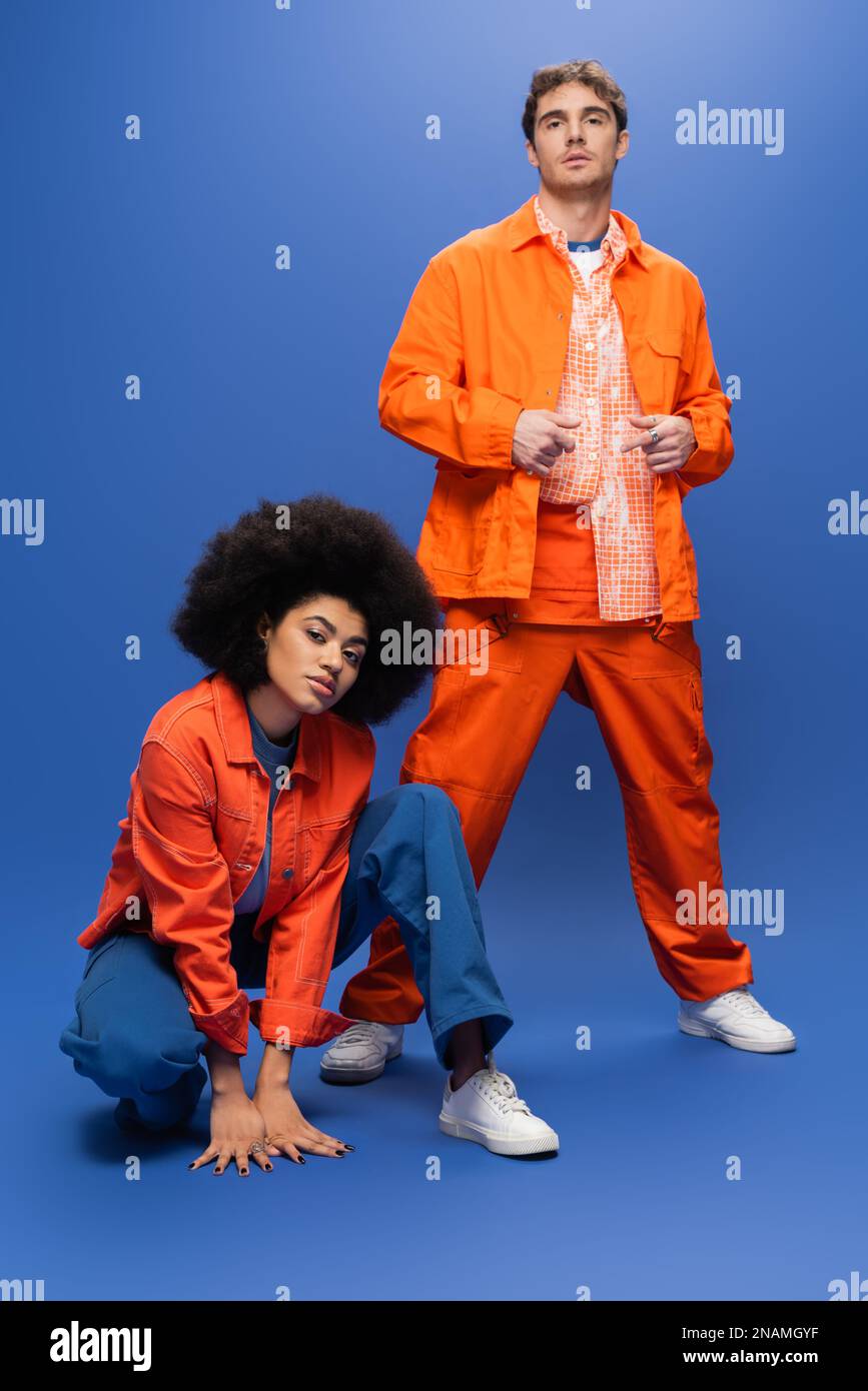 Selbstbewusste Modelle aus verschiedenen Rassen in orangefarbenen Jacken, die auf blauem Hintergrund auf die Kamera schauen, Stockbild Stockfoto