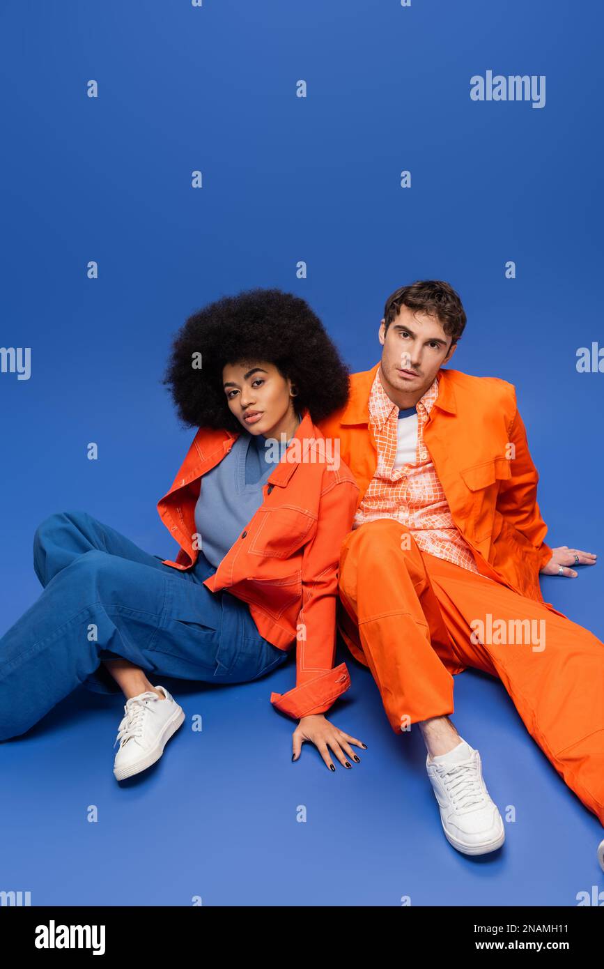 Multiethnisches Paar in orangefarbenen Jacken auf blauem Hintergrund, Stockbild Stockfoto