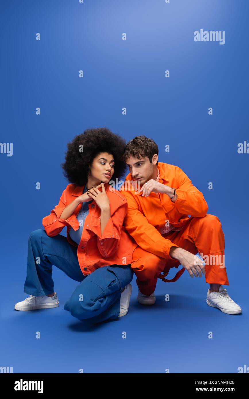 Ein junges, multiethnisches Paar in orangefarbenen Jacken, posiert auf blauem Hintergrund, Stockbild Stockfoto