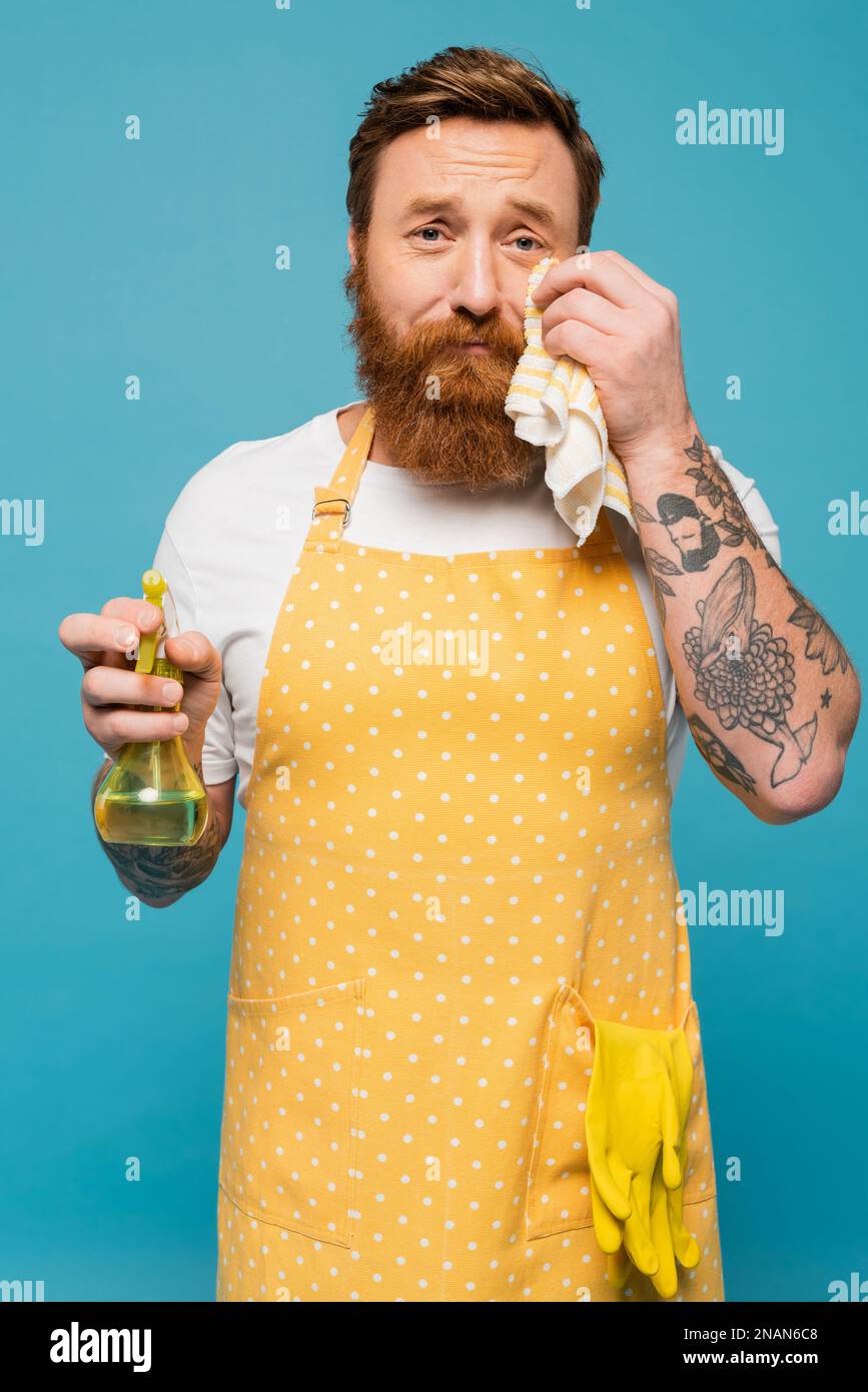 Weinender Mann mit Sprühflasche, wischte Tränen und schaute auf die Kamera, isoliert auf blauem Stockbild Stockfoto