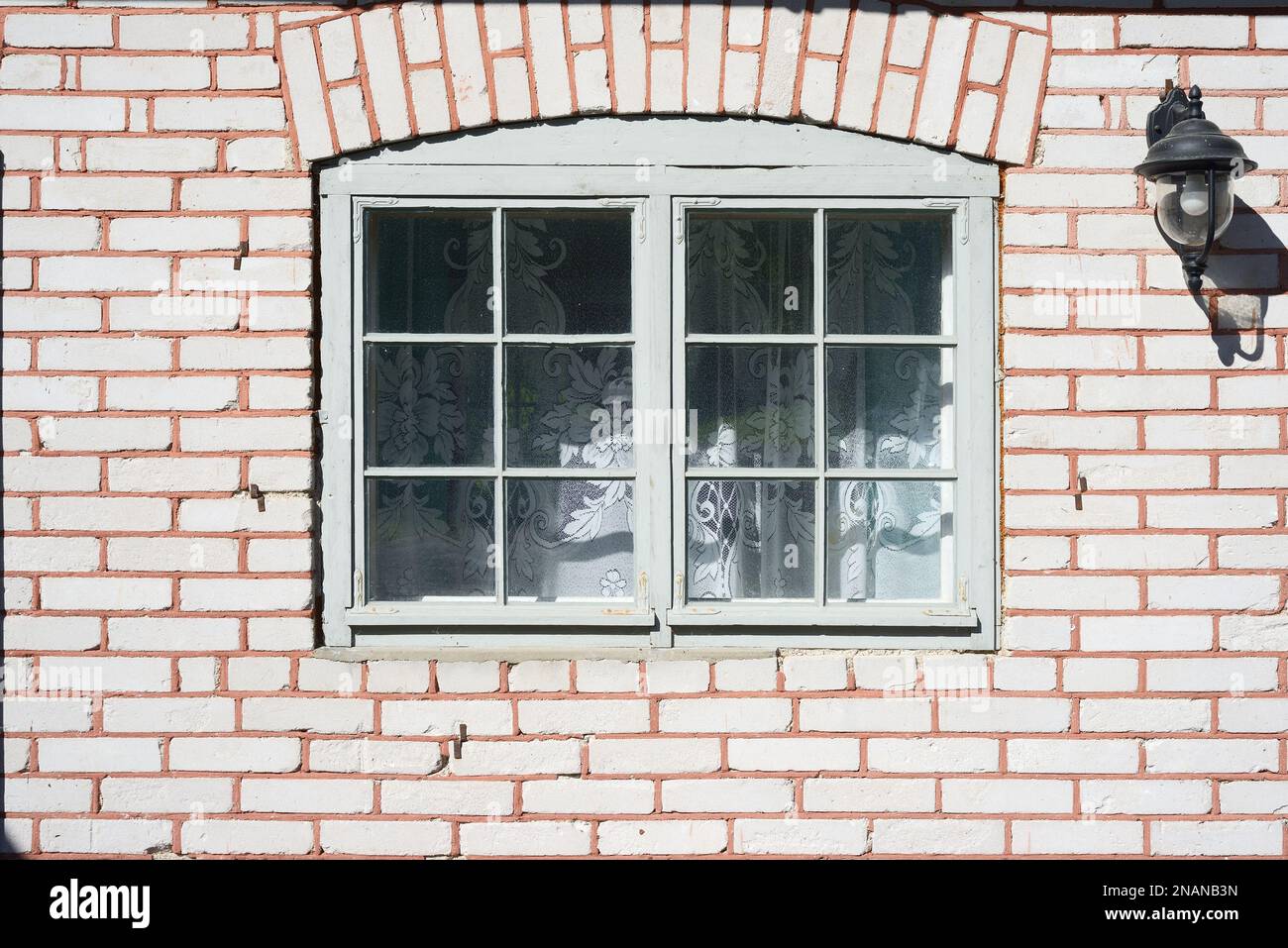 Altes Fenster in einem Ziegelhaus, Tulle-Vorhang und eine Laterne an der Wand Stockfoto