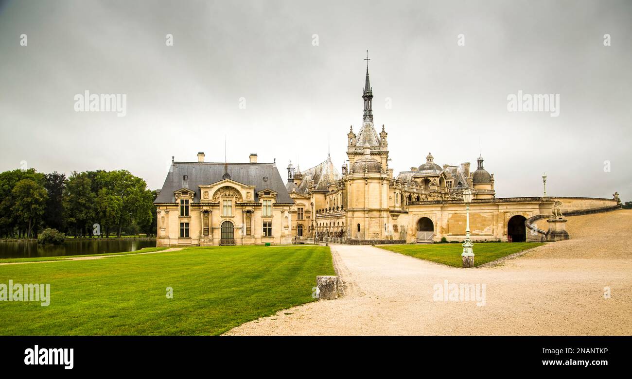 Chantilly, Frankreich, 08,26,2021: Panoramablick auf den Château de Chantilly, reflektiert im Wasser des Flusses mit hellen Wolken am Himmel. Stockfoto