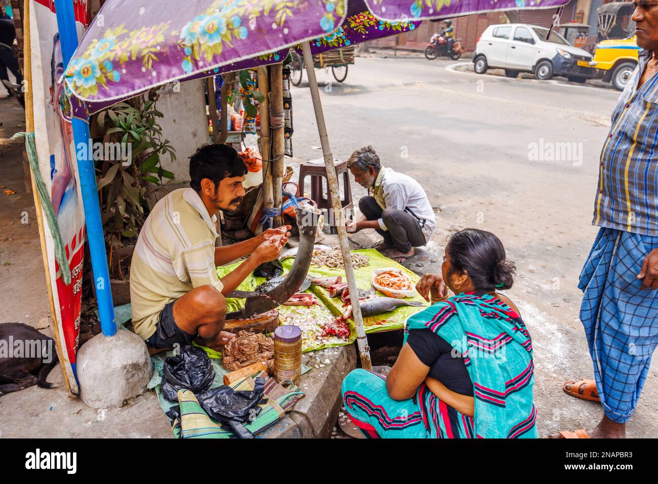 Einheimischer Straßenhalter entfernt Waagen, die Fisch für den Verkauf an einem typischen Straßenstand in Fariapukur, Shyam Bazar, Kalkutta, Westbengalen, Indien vorbereiten Stockfoto