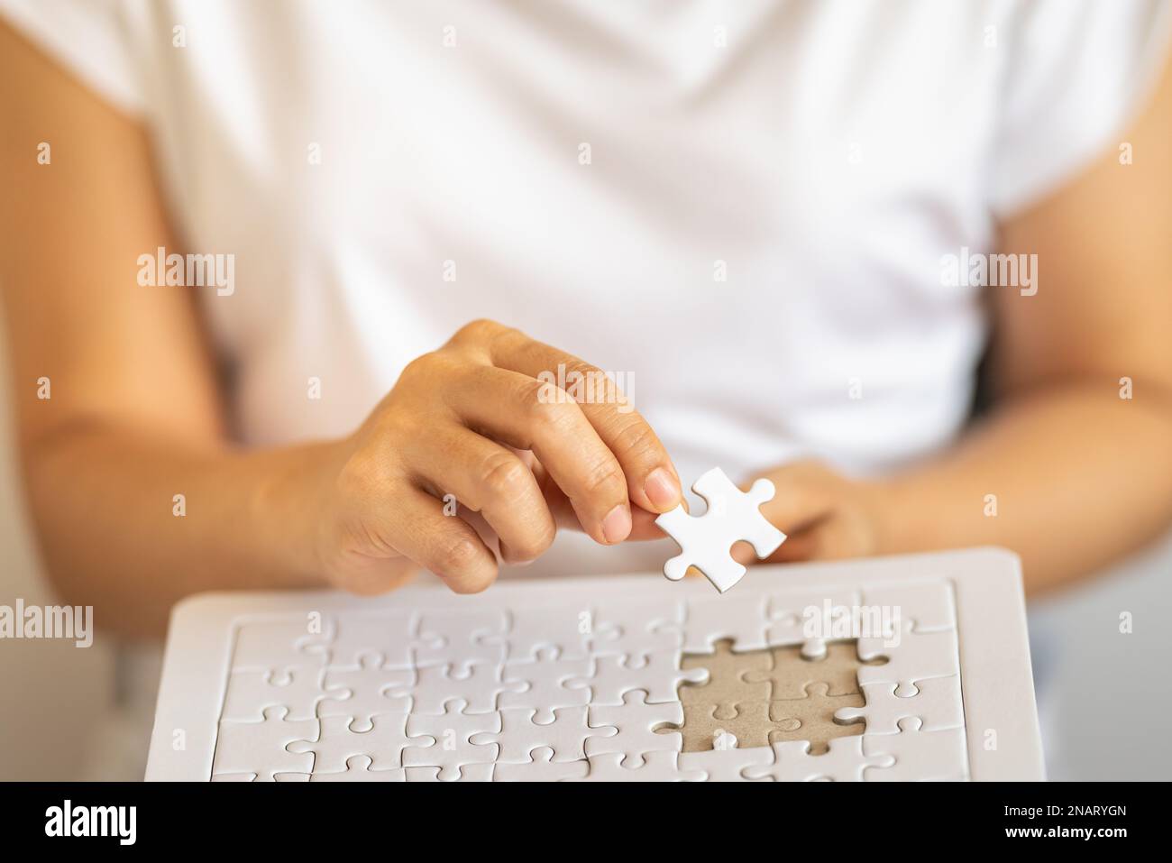 Nahaufnahme der Hand einer Frau, die ein Puzzle aus weißem Papier hält, und die Hand nach unten legt, um das Puzzle zu lösen. Verwendung als Business-Lösungen und Strategiekonzept. Stockfoto