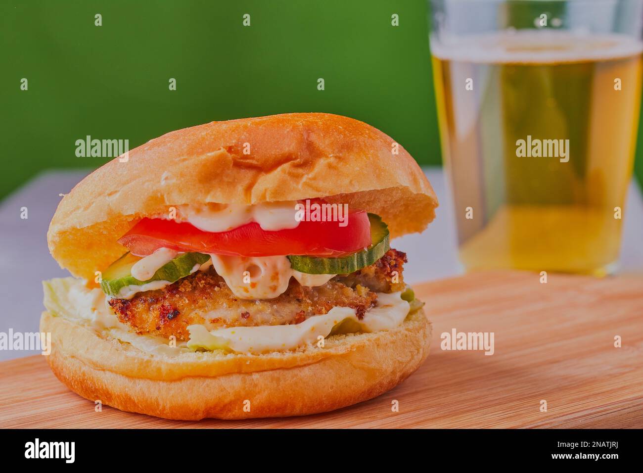 Leckerer Hähnchenburger mit einem Glas Bier im Hintergrund. Stockfoto