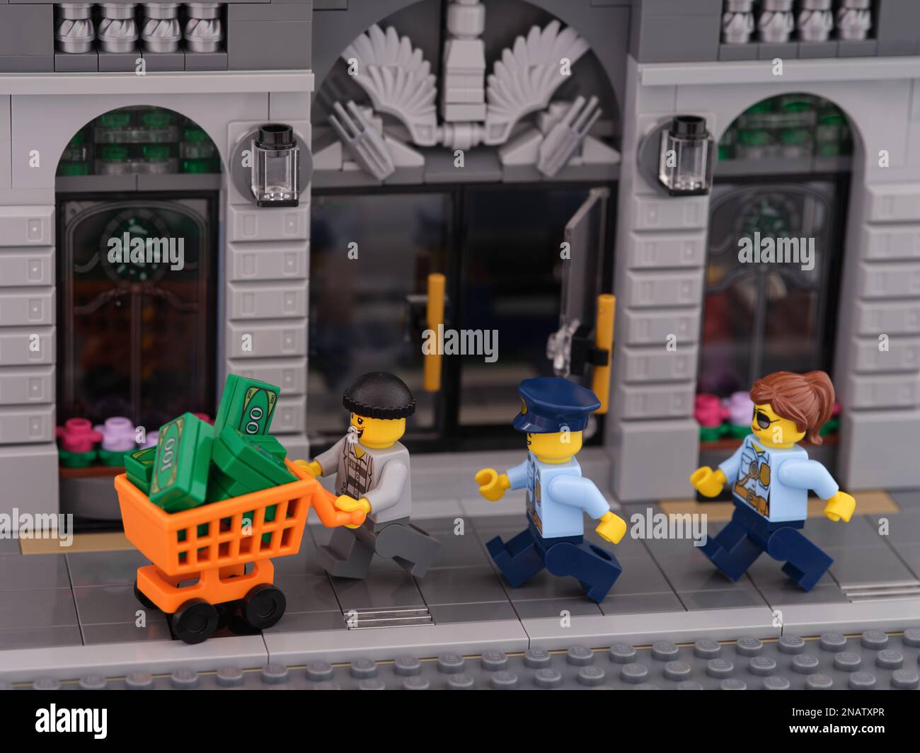 Tambov, Russische Föderation - 08. Februar 2023 Ein Lego-Dieb-Minifigure mit einem Einkaufswagen voller Geld, der vor zwei Polizisten Minifig wegläuft Stockfoto