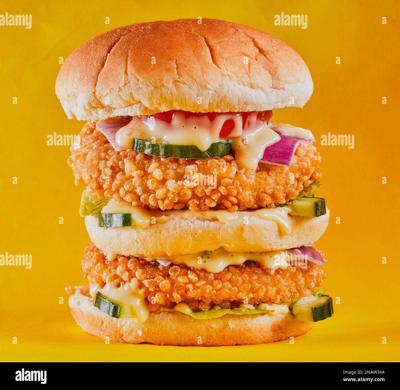 Köstlicher, doppelt gestapelter Hähnchenburger auf gelbem Hintergrund. Stockfoto