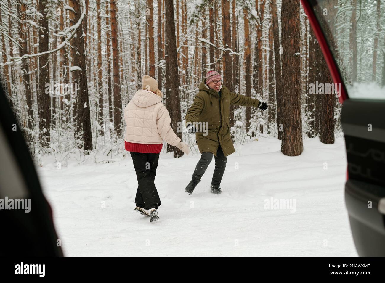 Fröhlicher, reifer Mann und Frau in Winterbekleidung, die Spaß in einem schneebedeckten Pinetree-Wald haben, während sie das Wochenende oder den Urlaub genießen Stockfoto