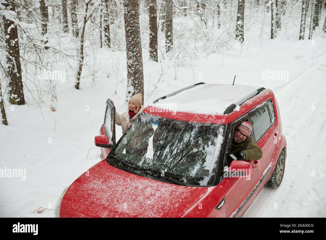 Glückliche Erwachsene Reisende, die aus ihrem Auto schauen und während des Wochenendausflugs einen wunderschönen Blick auf den Winterwald mit Schnee genießen Stockfoto