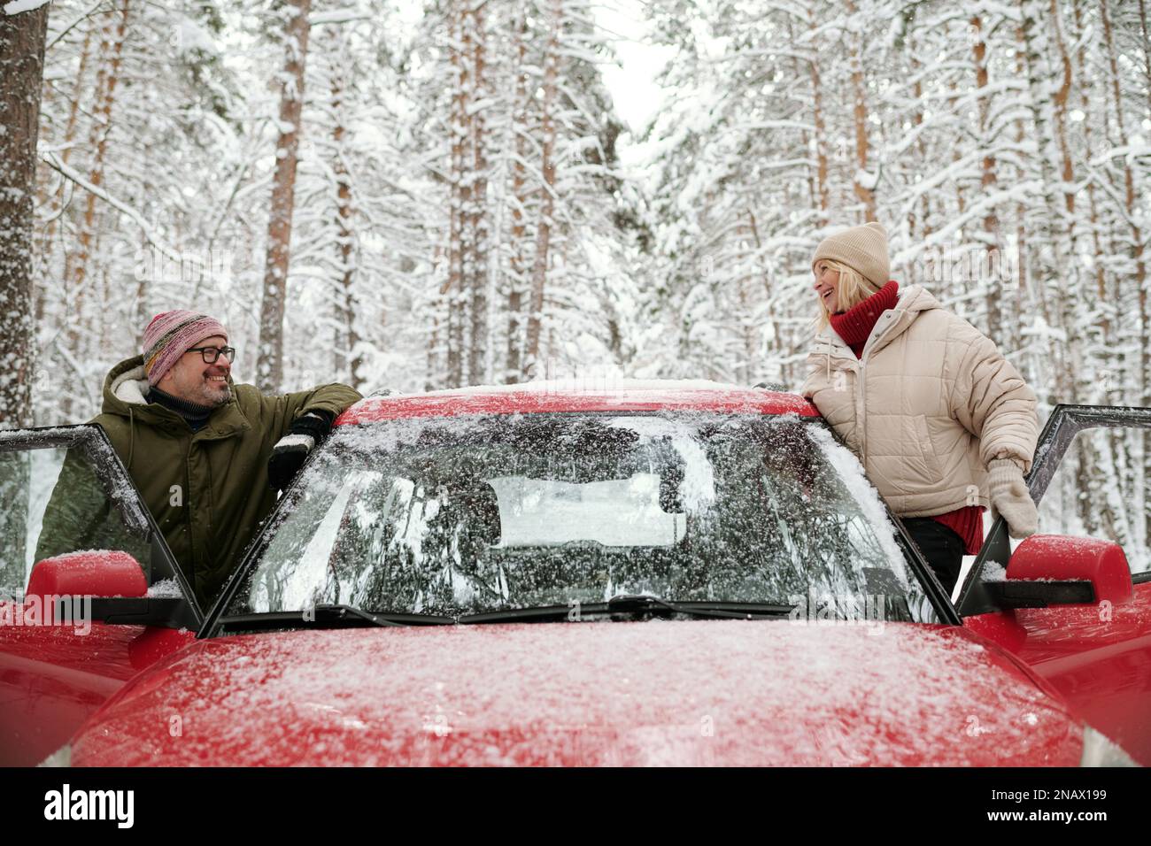 Zwei glückliche Erwachsene Menschen in Winterkleidung genießen das Winterwochenende oder den Urlaub im Pinetree Forest, während sie in offenen Türen des Autos stehen Stockfoto