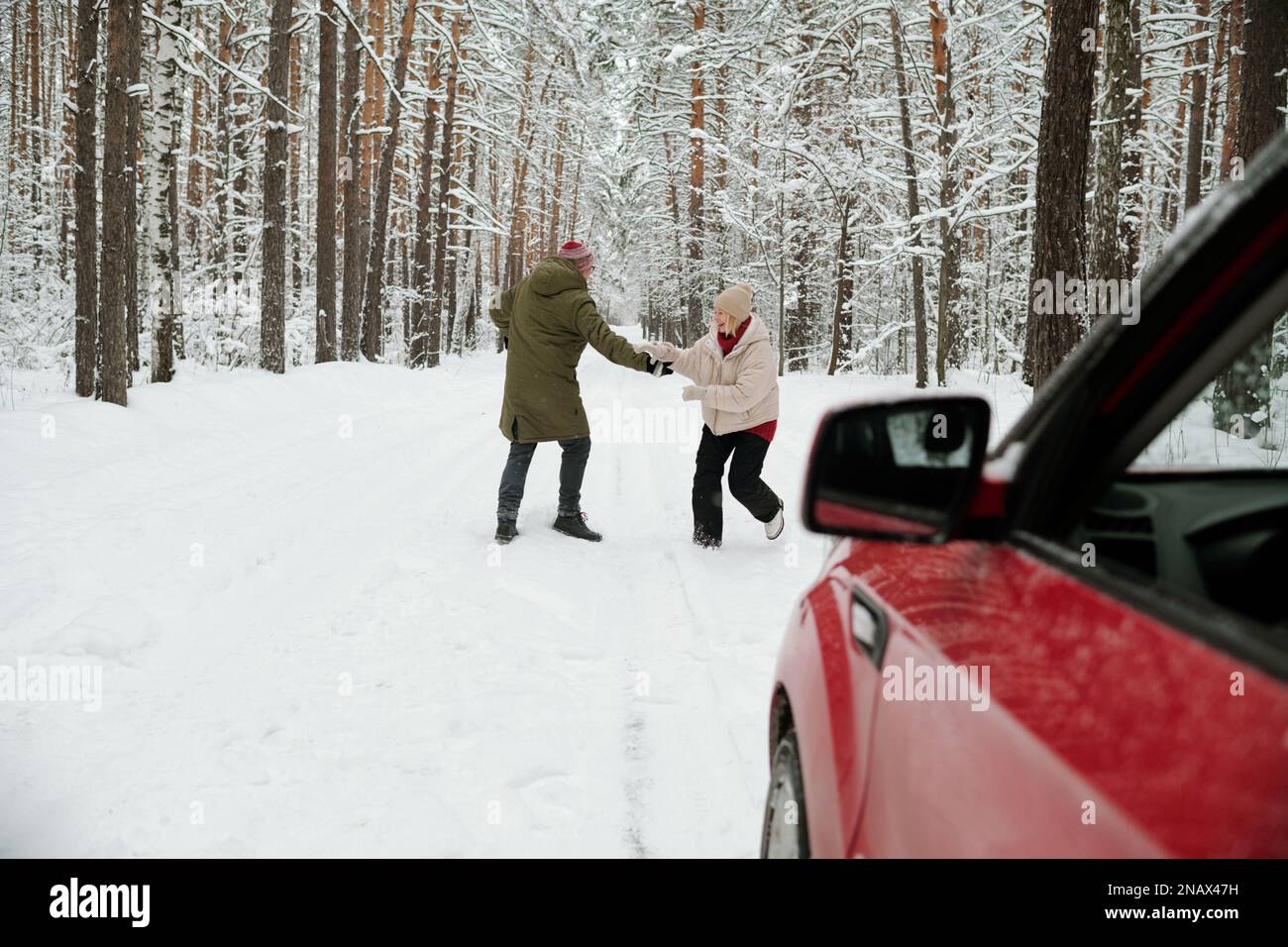Reifer Mann und Frau, die auf der Straße im schneebedeckten Pinienwald miteinander spielen und ihre Reise aufs Land genießen Stockfoto