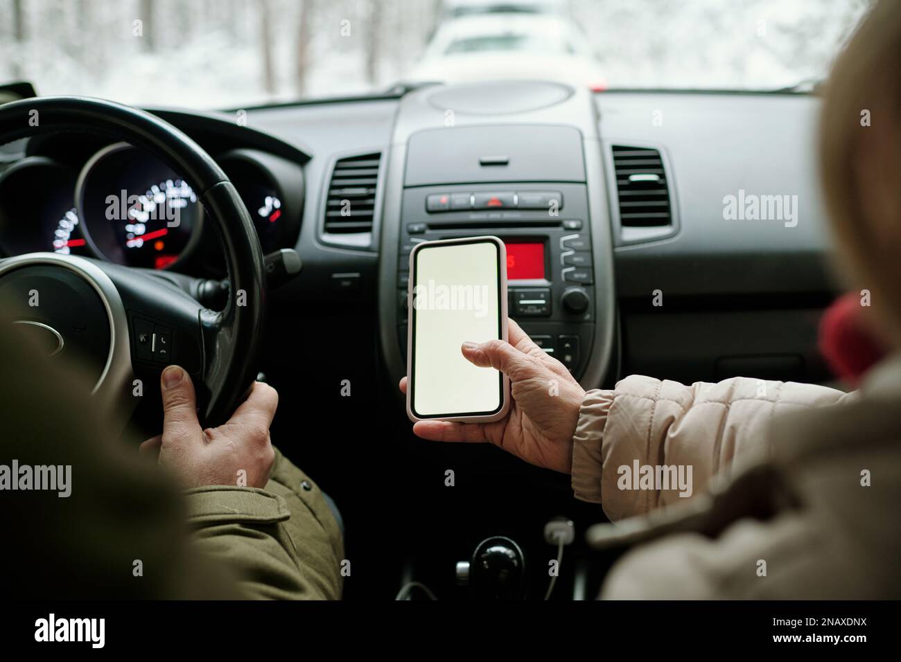 Nahaufnahme einer Seniorin, die ihr Smartphone mit leerem Bildschirm hielt, während sie im Auto neben ihrem Mann saß und während der Fahrt das Lenkrad hielt Stockfoto