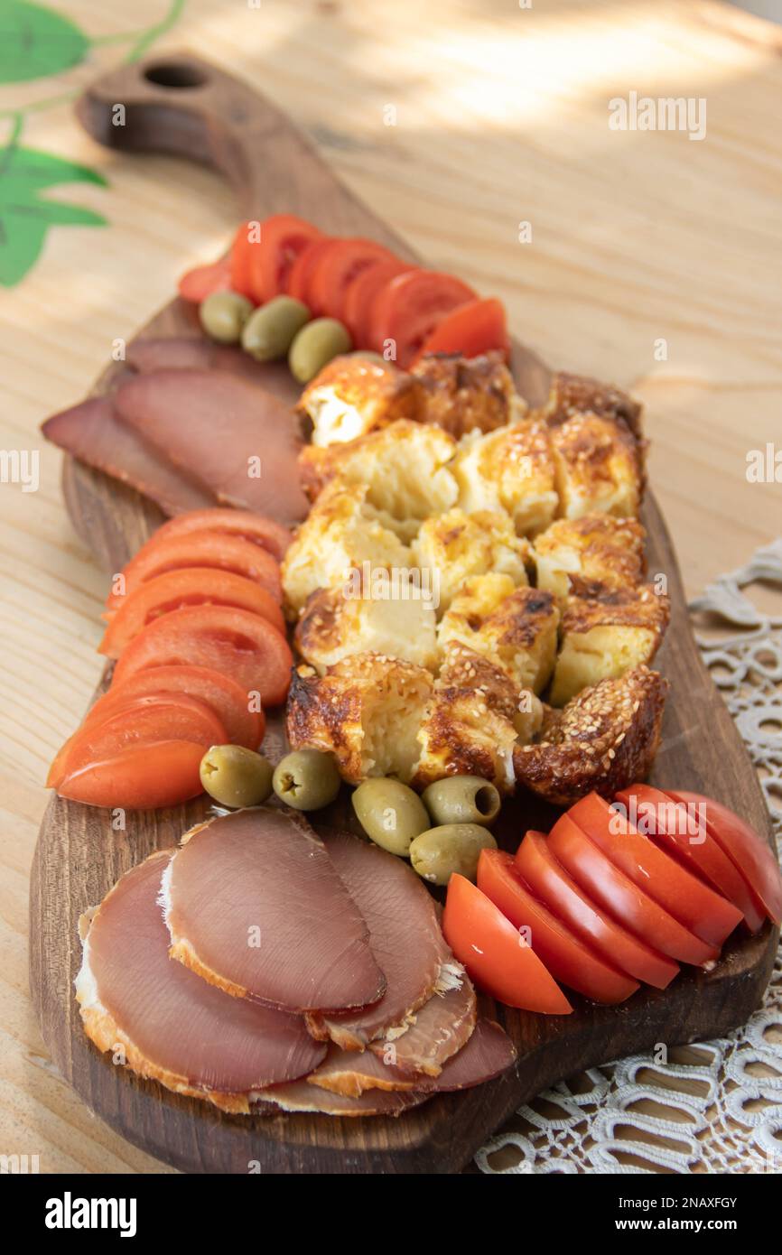 Serbische traditionelle Speiseplatte enthält Rind- und Schweinefleisch, getrocknete Meet, Käse, Gemüse und Proja-Brot aus Maismehl, serviert auf Holzteller Stockfoto