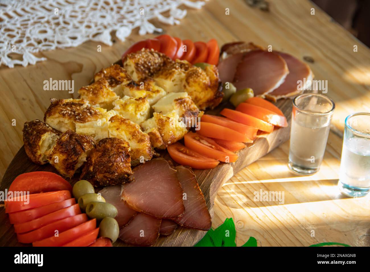 Serbische traditionelle Speiseplatte enthält Rind- und Schweinefleisch, getrocknete Meet, Käse, Gemüse und Proja-Brot aus Maismehl, serviert auf Holzteller Stockfoto