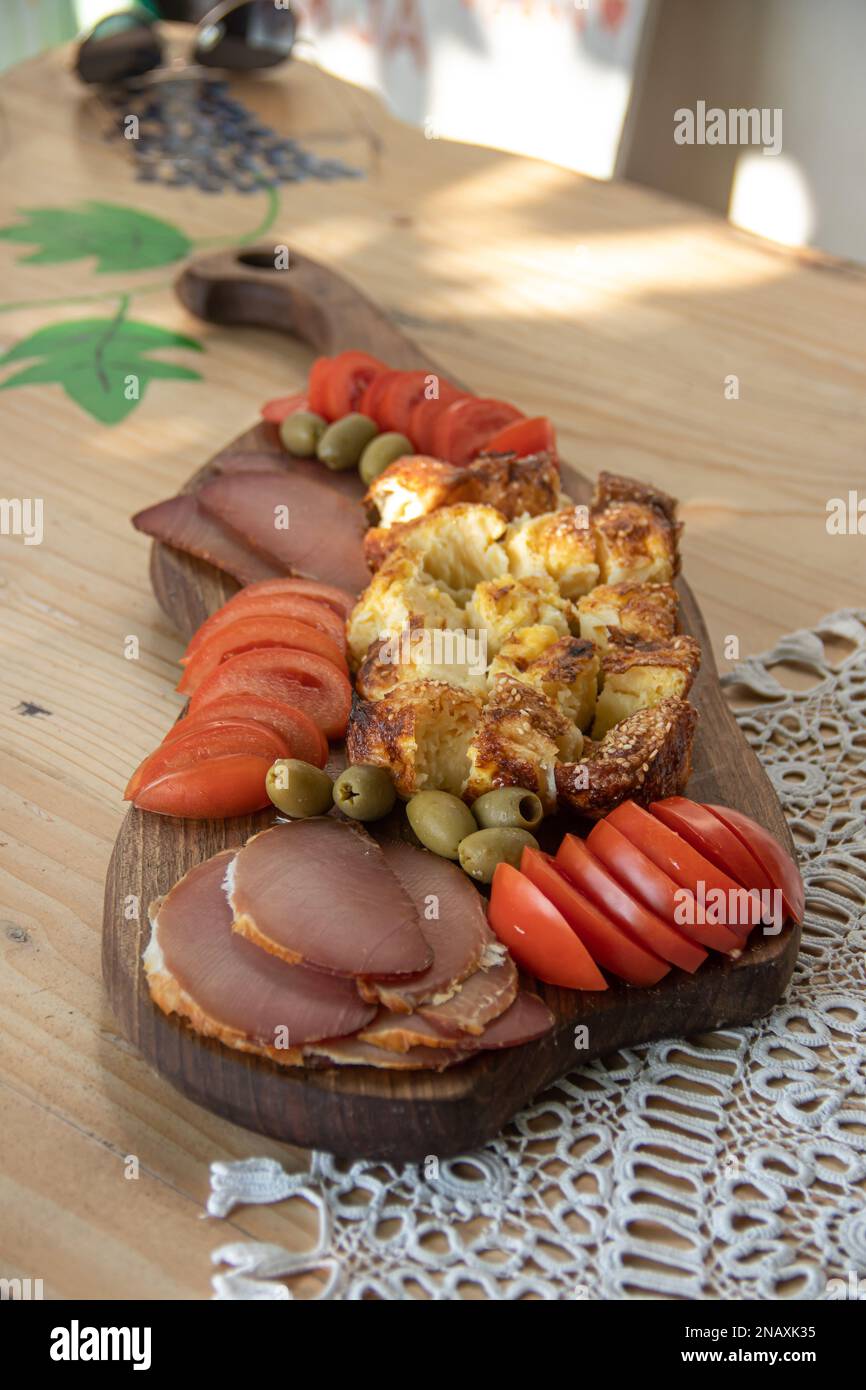 Serbische traditionelle Speiseplatte enthält Rind- und Schweinefleisch, getrocknete Meet, Käse, Gemüse und Proja-Brot aus Maismehl, serviert auf Holzteller Stockfoto