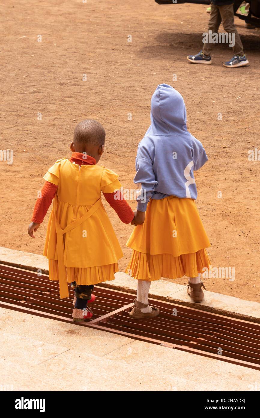 Karatu, Tansania - 16. Oktober 2022: Zwei Schwestern, die Händchen halten, während sie an einem sonntagmorgen aus dem Fenster der Karatu-Kirche Tansania treten. Stockfoto