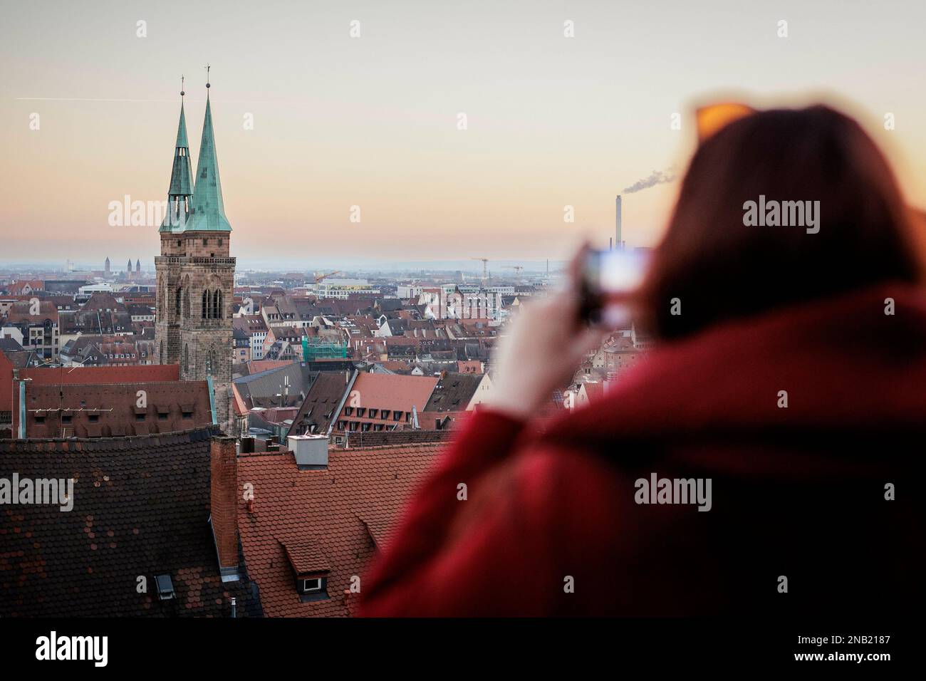 Nürnberg, Deutschland. 13. Februar 2023. Eine Frau macht ein Foto von Nürnberg mit ihrem Handy bei Sonnenuntergang mit der Sebalduskirche. Nürnberg, 13. Februar 2023. Kredit: dpa/Alamy Live News Stockfoto