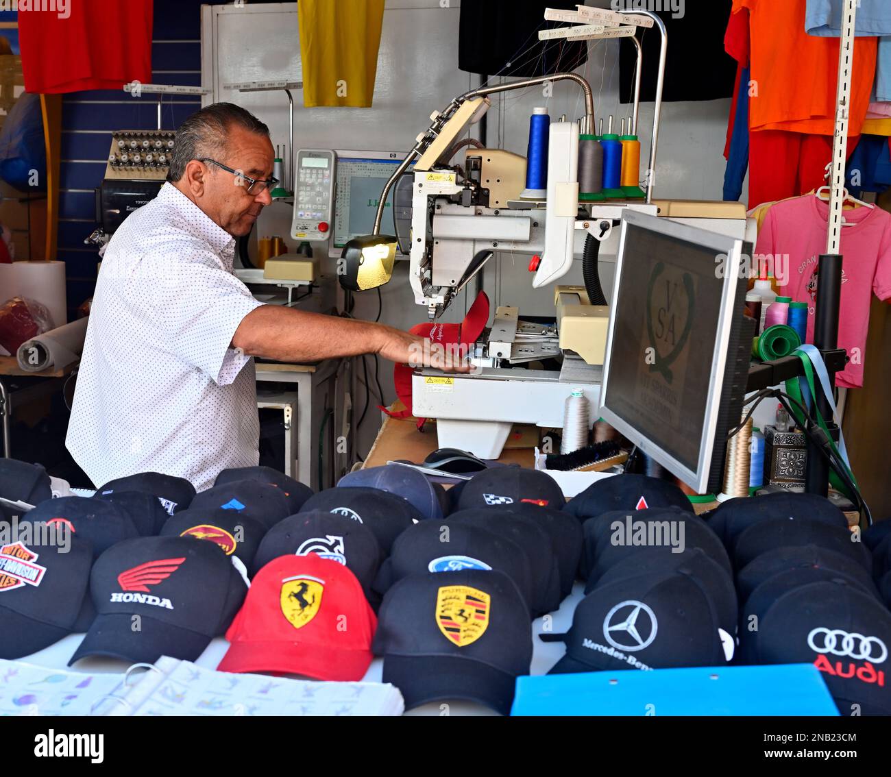 Mehrfarbige sechs-Kopf-Stickerei zwölf Nadeln gewerbliche Stickerei Maschine Logo auf Hut im Touristenzentrum von Maspalomas, Gran Canaria Stockfoto