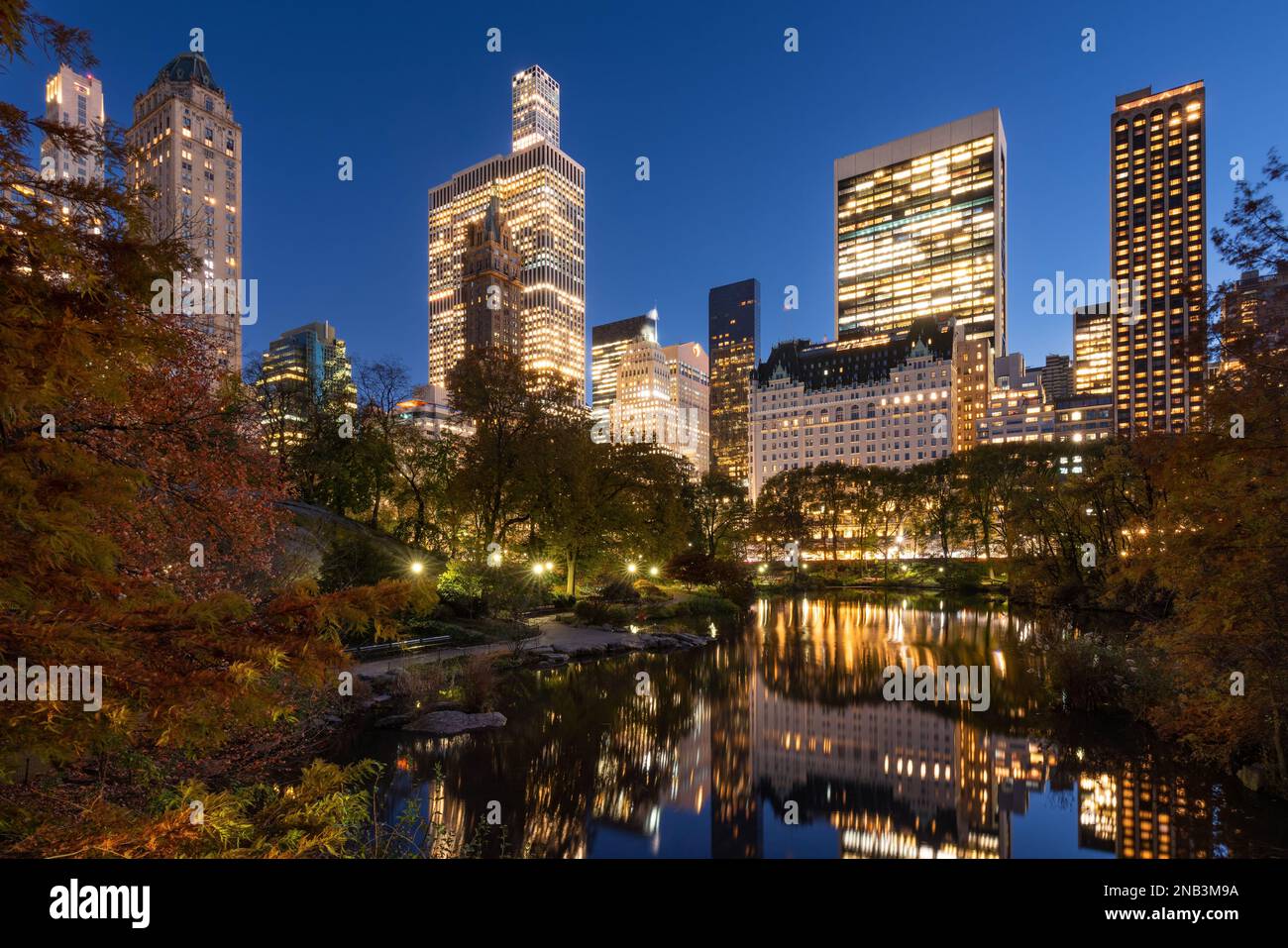 Beleuchtete Wolkenkratzer in Manhattan am Abend und der Teich im Central Park. In New York City Stockfoto