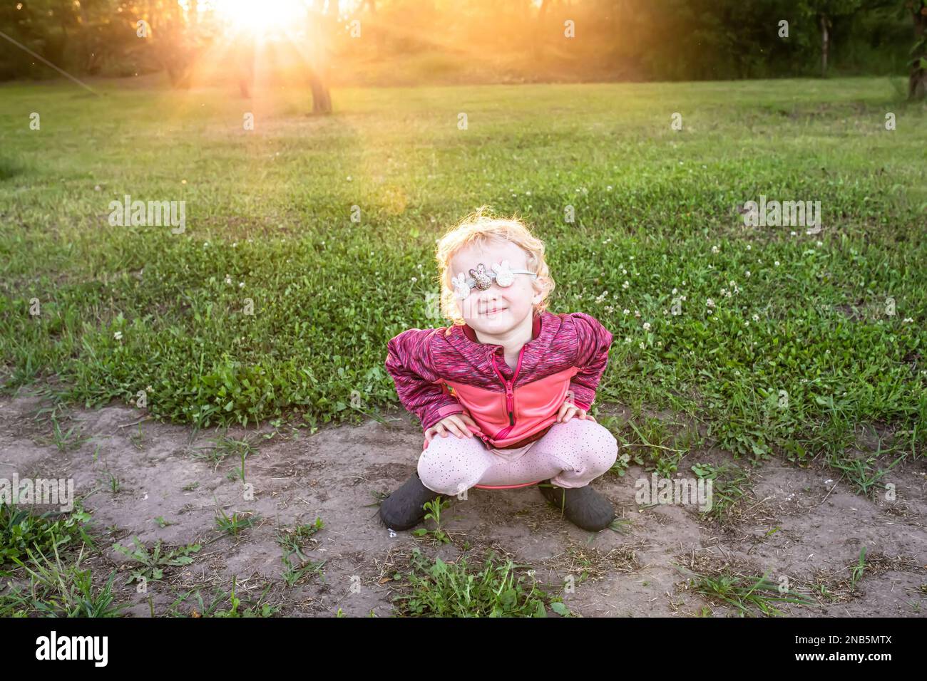 Ein kleines Kind missbilligt das Sitzen und Hocken bei Sonnenuntergang. Das Mädchen schloss ihre Augen mit einer Augenbinde Stockfoto
