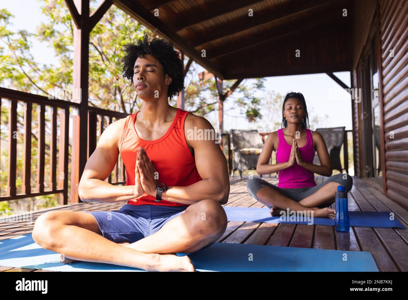 Ein afroamerikanisches Paar, das in einer Blockhütte Yoga auf Yoga-Matten praktiziert. Blockhütte, Natur- und Lifestyle-Konzept. Stockfoto