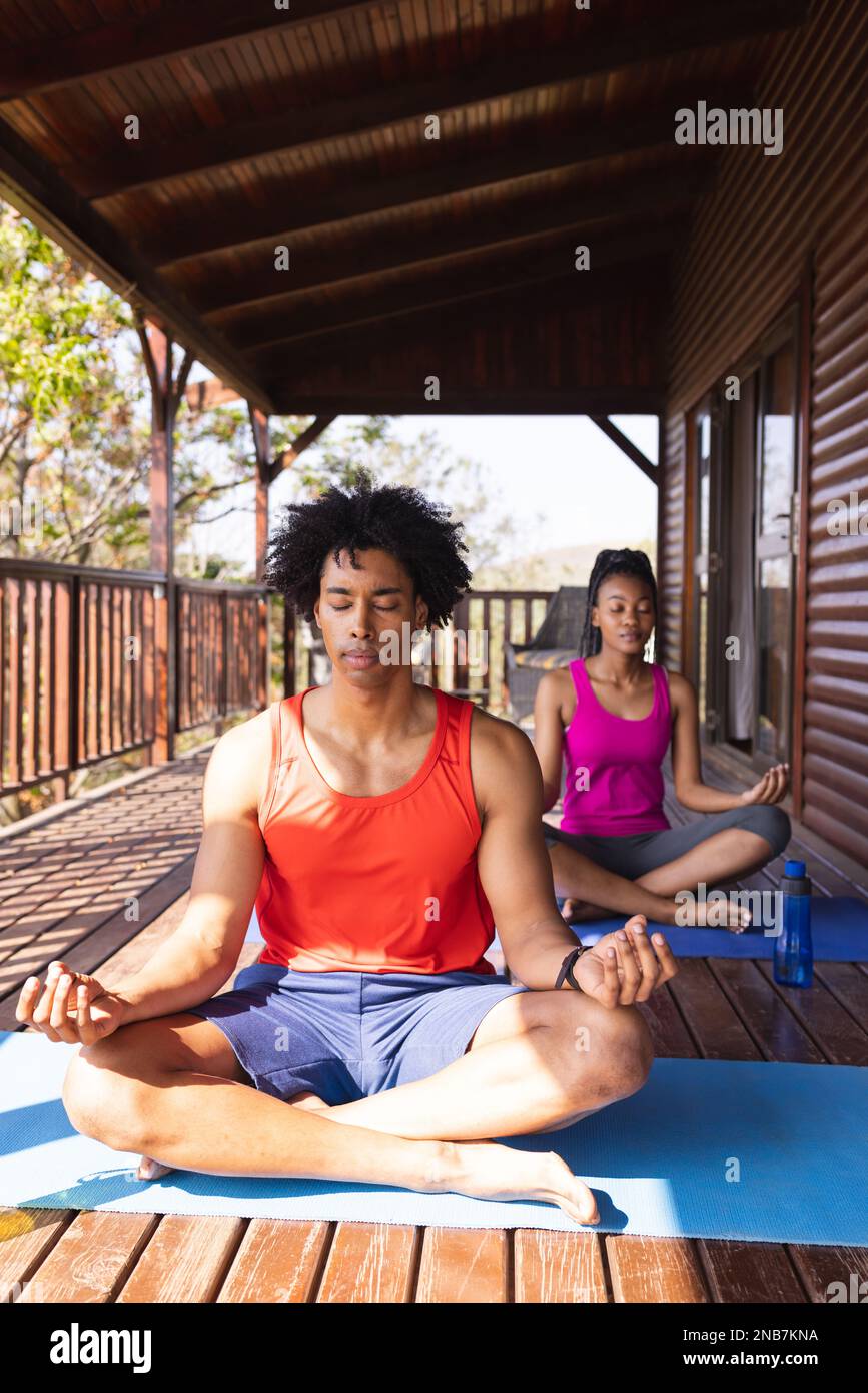 Ein afroamerikanisches Paar, das in einer Blockhütte Yoga auf Yoga-Matten praktiziert. Blockhütte, Natur- und Lifestyle-Konzept. Stockfoto
