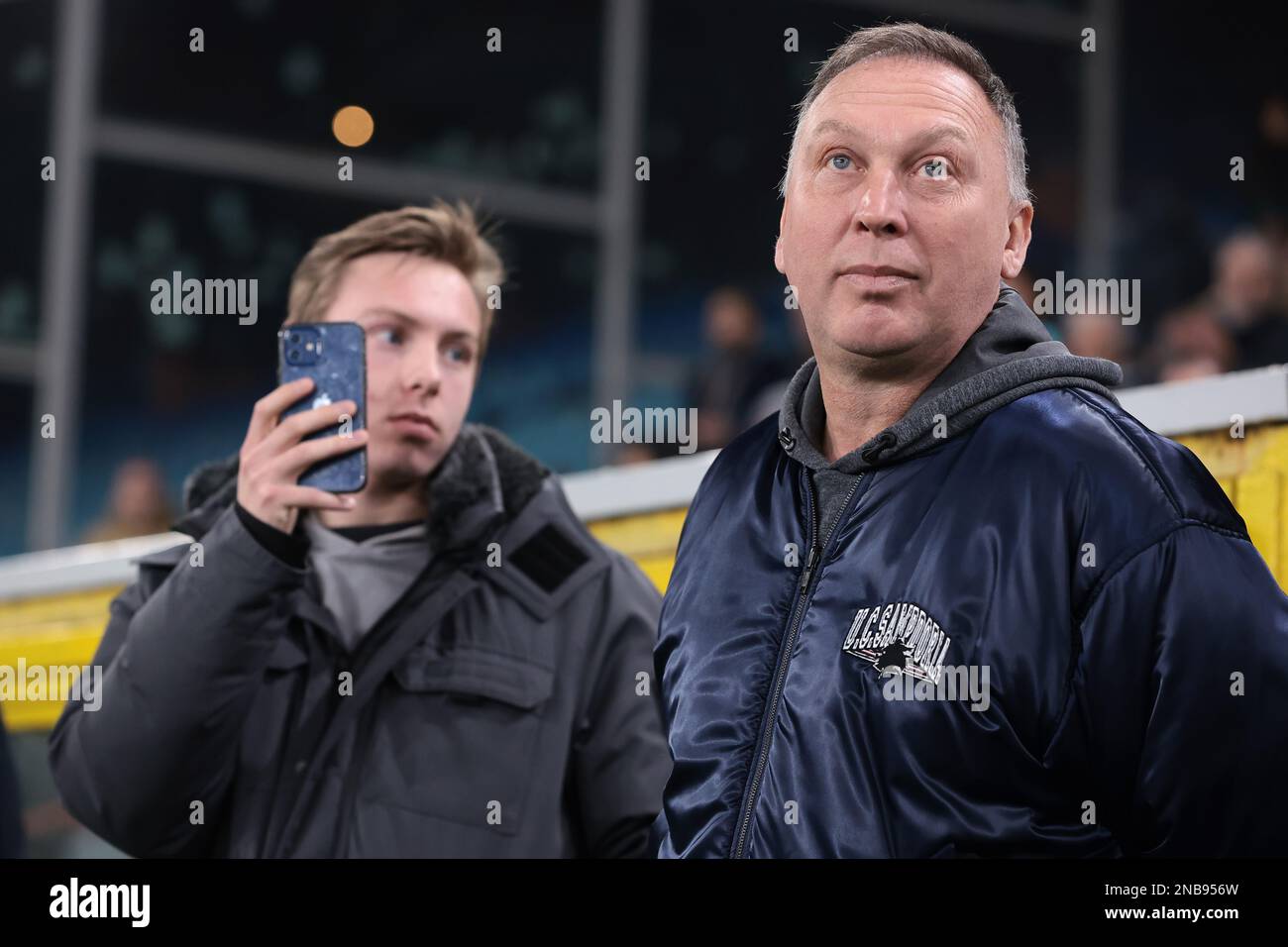 Genua, Italien, 13. Februar 2023. Ehemalige Crewe Alexandra, Aston Villa, Bari, Juventus, Sampdoria, Der Spieler David Platt, Arsenal, Nottingham Forest und England, schaut zu, während sein Sohn Charlie mit einem Smartphone Aufnahmen macht, während Bilder seiner Karriere in Genua vor dem Spiel der Serie A in Luigi Ferraris, Genua, auf die Leinwand des Stadions projiziert werden. Der Bildausdruck sollte lauten: Jonathan Moscrop/Sportimage Stockfoto