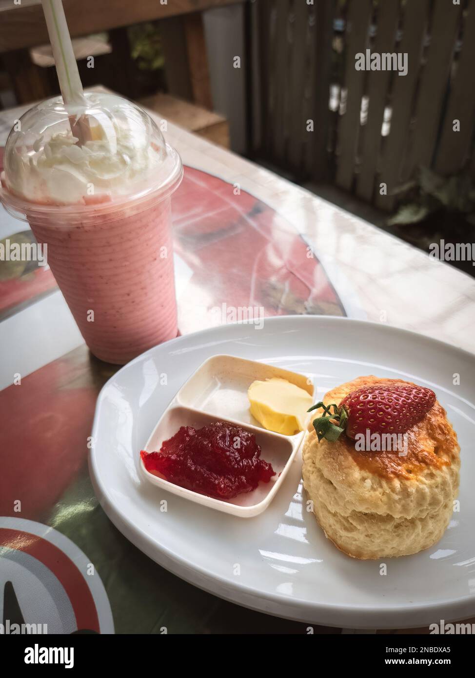 Scones auf einem weißen Teller mit Erdbeermarmelade und eine Tasse Erdbeermilchshakes im Hintergrund Stockfoto