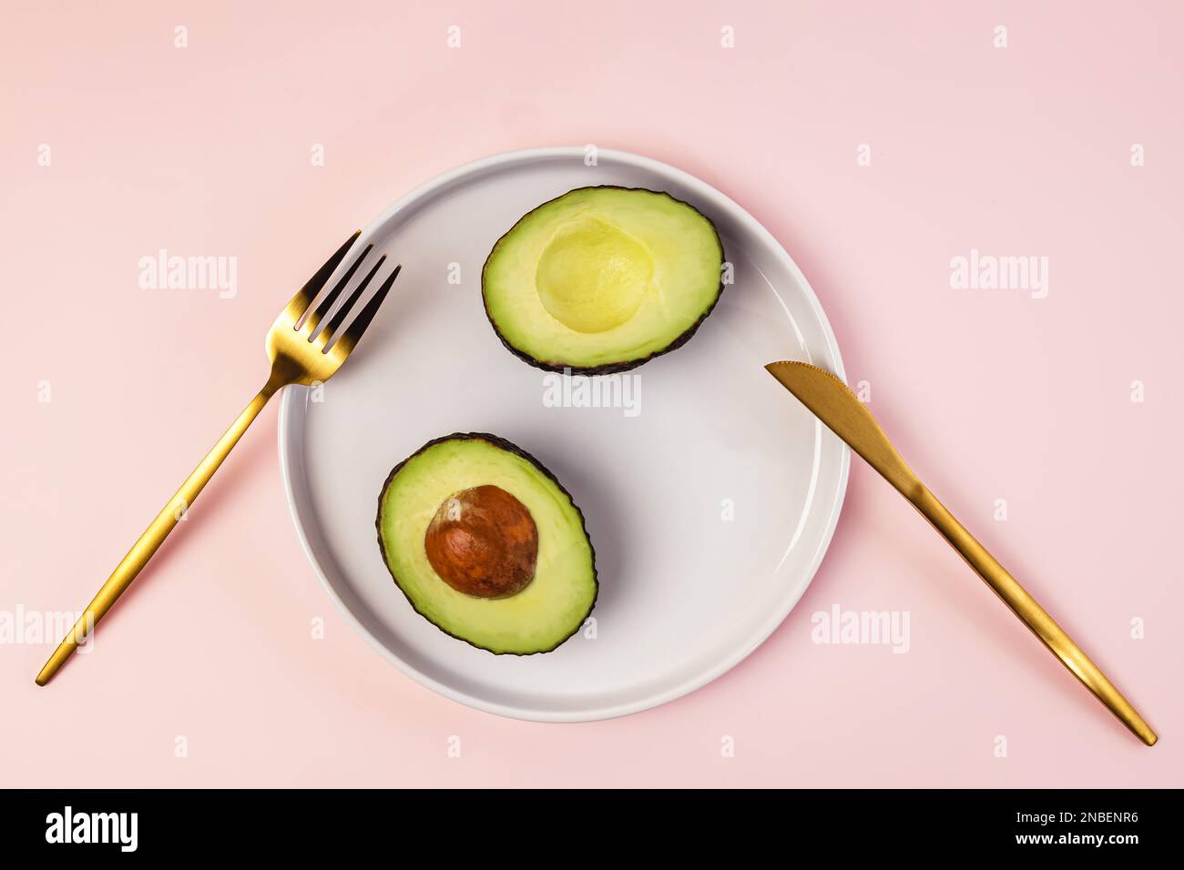 Avocado in Hälften auf dem Teller geschnitten und goldfarbenes Besteck, Draufsicht Stockfoto