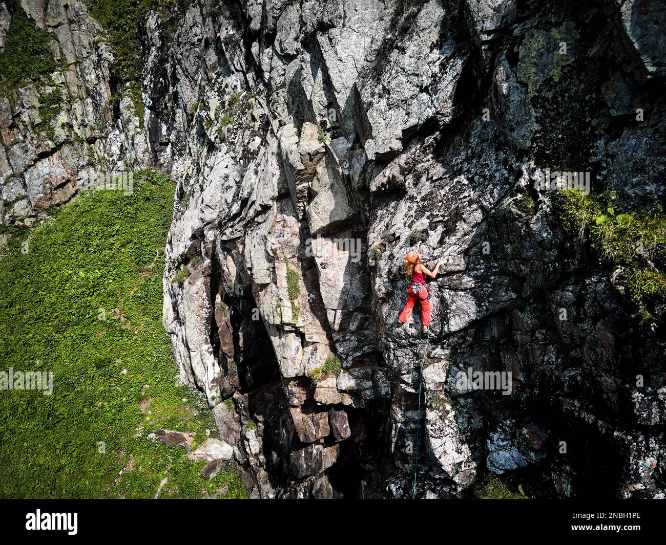 Drohnenaufnahme einer starken Frau im roten Hemd, die auf dem hohen Felsen in den Bergen Tyan Shan in Kasachstan klettert Stockfoto